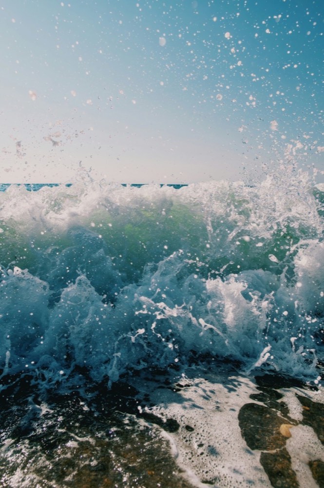 A wave breaking hard against dark rocks, spray bursting upward